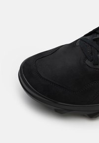 Svart mocka sko med en texturerad ovandel, platta snören och en rundad gummisula. Har subtila sömdetaljer och en strömlinjeformad design.