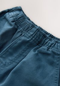 Šortky zo zmesi bavlny s elastickým pásom, vyrobené z textúrovanej tmavomodro-zelenkavej látky, hladkým povrchom a starostlivým prešívaním pozdĺž okrajov.