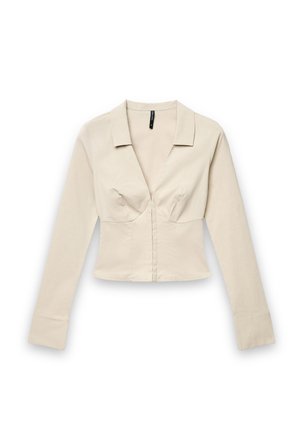 Blouse beige ajustée à manches longues avec un col en V profond, un col et des détails structurés au niveau du buste sur un fond blanc.