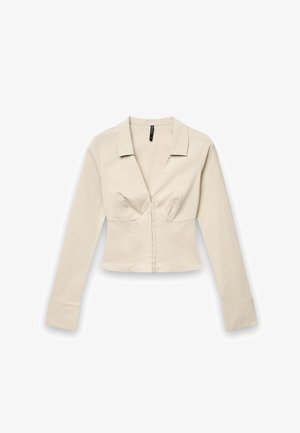 Blouse beige ajustée à manches longues avec un col en V profond, un col et des détails structurés au niveau du buste sur un fond blanc.