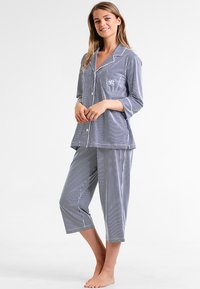 Sininen ja valkoinen raidallinen pyjama-asusarja, jossa on napitettava paita ja lyhyet housut. Sisältää rintataskun ja pehmeän kangasrakenteen.