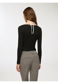 Maglietta nera a maniche lunghe con dettaglio in bianco al collo; abbinata a pantaloni grigi con tasche laterali e una vestibilità sartoriale.