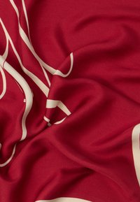 Punainen kangas, jossa on sileä rakenne ja rohkeita kermaista abstraktia kuvioita. Materiaali näyttää kevyeltä ja laskeutuu pehmeästi.