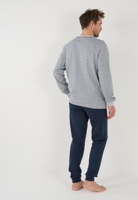 Maglietta a maniche lunghe con un motivo geometrico blu e bianco, abbinata a pantaloni blu scuro, entrambi realizzati in un tessuto morbido. Nessun logo o dettaglio visibile.