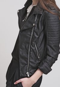 Giubbotto da moto in pelle nera con design cropped, zip argento, dettagli a coste sulle spalle e una texture leggermente consumata.