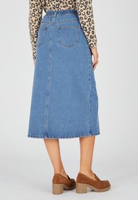 Falda de mezclilla en corte A de color azul claro con cinturilla fruncida y dos bolsillos traseros. Combinada con zapatos de tacón de ante marrón.