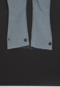 Pantalones de mezclilla de un tono azul claro, con bordes sin rematar en el dobladillo, acentuados con dos botones negros redondos a cada lado.