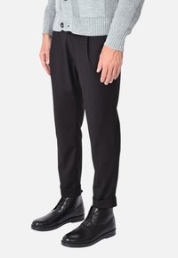 Cardigan grigio a coste sopra un paio di pantaloni neri aderenti, completato da stivali in pelle nera. Design compatto con dettagli sottili sugli indumenti.