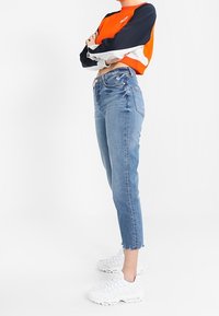 Jeans in denim con orlo sfrangiato, lavaggio blu chiaro; abbinati a un maglione cropped in color block arancio e blu navy. Sneakers bianche.