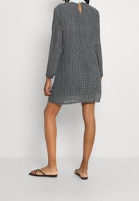 Grå långärmad klänning med strukturerad yta, med ett nyckelhål i ryggen, och stylingen kompletteras med svarta platta sandaler.