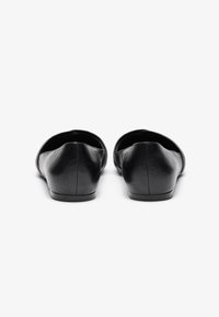 Zapatos planos de cuero negro con punta redondeada y diseño minimalista. Textura lisa con un tacón bajo y discreto. Sin herrajes ni acentos visibles.