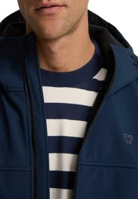 Chaqueta con capucha de color azul marino con cremallera, que presenta una textura suave y dos bolsillos frontales, llevada sobre una camiseta de rayas blanca y azul marino.
