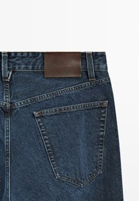 Jeans in denim blu scuro con etichetta in pelle marrone in vita e design con tasca posteriore accentuata da cuciture a contrasto.