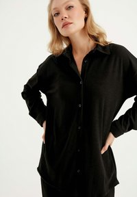 Schwarzes, geripptes Hemd mit Knöpfen, Kragen, langen Ärmeln und lockerem Schnitt. Verfügt über einen abgerundeten Saum und schwarze Knöpfe. Weicher Stoff.