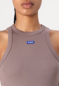 Ärmlös ribbad linne i dämpad mauve, med en blå "HUGO" logotyp på bröstet, med en figurnära silhuett och hög hals.