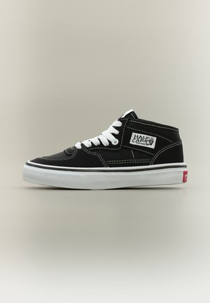 Čierno-biela skate topánka Vans Half Cab s bielymi šnúrkami, bielou medzipodrážkou a viditeľnou značkovou nášivkou na boku na neutrálnom pozadí.