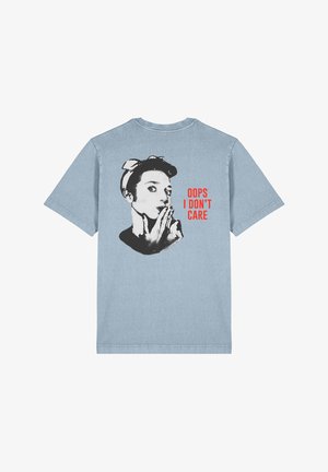 T-shirt bleu clair à manches courtes avec un graphique noir et blanc d'une femme portant un bandeau, texte en rouge : "OUPS JE M'EN FICHE."