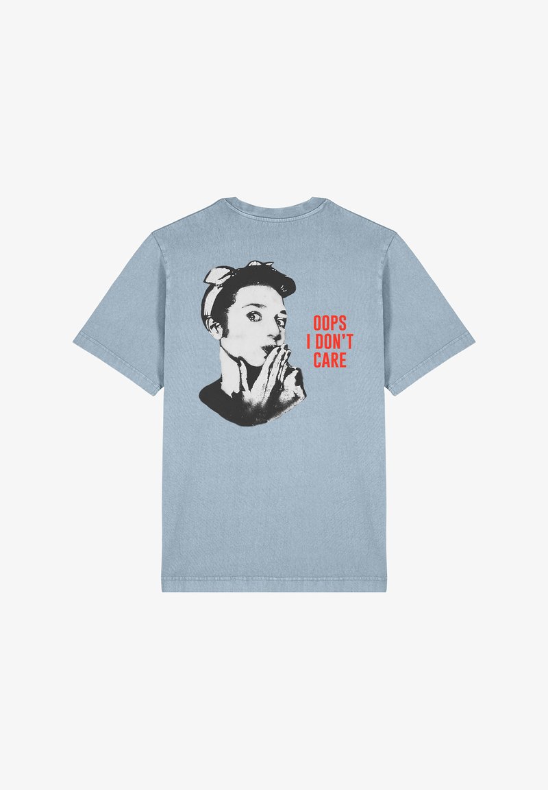 T-shirt bleu clair à manches courtes avec un graphique noir et blanc d'une femme portant un bandeau, texte en rouge : "OUPS JE M'EN FICHE."