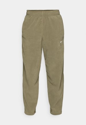 Pantaloni jogger in pile verde oliva con vita elastica. Presentano un piccolo logo bianco vicino alla tasca e un design a gamba affusolata. Texture morbida.