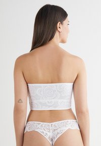 Vit spets bandeau-topp och matchande tanga, prydd med blommönster och en slät yta, designad utan remmar för en sömlös look.
