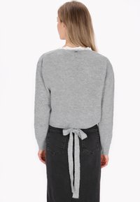 Maglione grigio lavorato a maglia con una vestibilità morbida, caratterizzato da un dettaglio con lacci sulla schiena, abbinato a una gonna in denim nera. Texture morbida e design semplice.