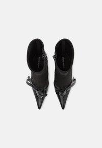 Botine negre până la gleznă, cu vârf ascuțit. Făcute din suede și piele, cu un accent sub formă de fundiță pe lateral și închidere cu fermoar pentru o îmbrăcare ușoară.