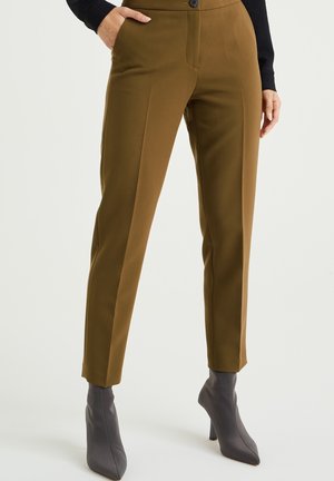 Hnědé kalhoty na míru se slim fit střihem, vyrobené z hladké tkaniny, s předními kapsami a knoflíkovým zapínáním, v kombinaci se šedými kotníkovými botami.