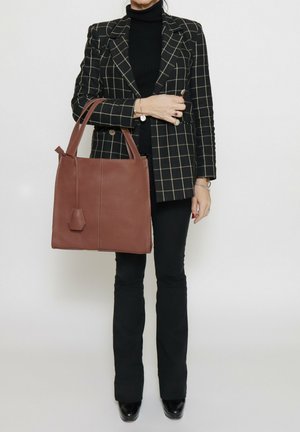 Braune Ledertasche mit strukturiertem Design, zwei kurzen Griffen und einem hexagonalen Akzent an der Seite, vor einem neutralen Hintergrund.