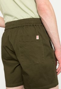 Olijfgroene shorts van katoen met een elastische tailleband, voorzien van een enkele achterzak en een klein logo label.