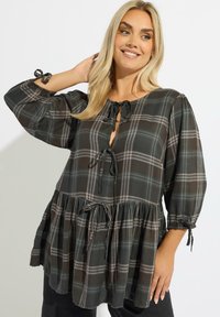 Blusa de cuadro negro y verde con mangas de globo de tres cuartos, escote con lazo y un dobladillo acampanado y fruncido, que presenta detalles con cordón.