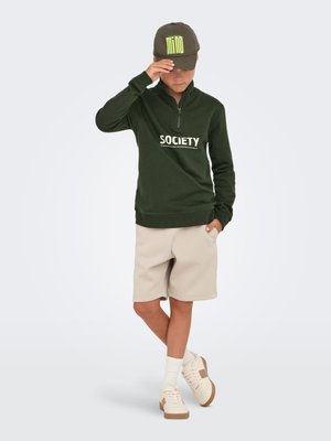 Olive green zip-up sweatshirt with "SOCIETY" text, beige shorts, white socks, and beige sneakers. The cap is dark green with neon logo.