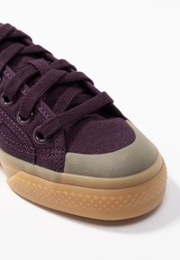 Fialový plátěný teniska s texturovanou gumovou špičkou, zavazováním na tkaničky, zesílenými průchodkami a gumovou podrážkou s geometrickým vzorem.
