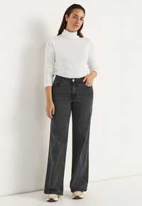 Svarta vida jeans med hög midja, kombinerade med en figurnära vit polotröja. Slät textur, klassisk design och synliga framfickor.