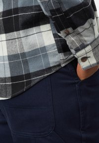 Geruit flanellen overhemd in grijs, zwart en wit met knoopmanchetten, gecombineerd met marineblauwe stoffen broek met een zijzak en een textuurrijke afwerking.