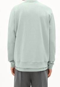 Mintunvihreä collegepaita pyöreällä pääntiellä, pitkät hihat, resorit hihoissa ja helmassa, valmistettu pehmeästä puuvillasekoitteesta. Yksinkertainen, koristeeton malli.