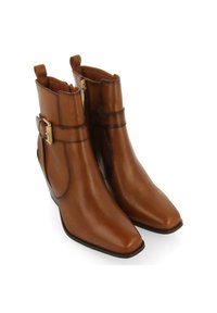 Botas de cuero marrón hasta el tobillo con puntera puntiaguda, cremallera lateral y detalle de hebilla en tono dorado. Textura suave y silueta elegante.