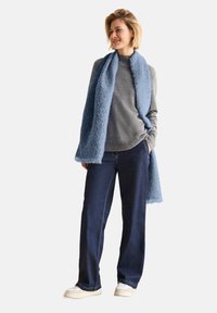 Una bufanda azul claro, un suéter gris y unos jeans de pernera ancha azul oscuro. La bufanda tiene una textura suave y bordes con flecos. Unos sneakers casuales completan el look.