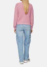 Pull en maille texturé rose avec un design court, associé à un jean cargo bleu clair avec poches latérales et coupe décontractée.