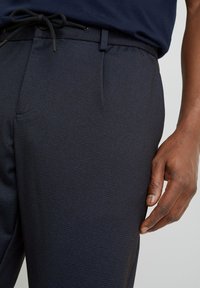 Pantalon bleu marine à motif, doté d'une ceinture élastique avec cordon de serrage, de poches latérales et d'une texture de tissu lisse.