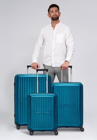 Drei ineinandergreifende Koffer in Teal-Farbe mit vertikaler Rillenstruktur, Hartschale, ausziehbaren Griffen und 360-Grad-Rädern.