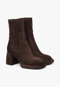 Hnědé semišové kotníkové boty s blokovým podpatkem, zaoblenou špičkou, elastickými bočními panely a prošívanými detaily v horní části. Hladký, strukturovaný povrch.