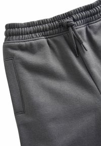 Pantalones de chándal grises hechos de una suave tela texturizada. Cuenta con una cinturilla elástica con cordón y un bolsillo lateral.