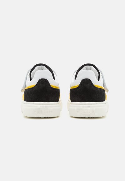 Sneaker in suede nero e pelle bianca con una striscia di accento gialla, colletto imbottito e suola in gomma bianca testurizzata.