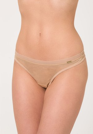 String en dentelle beige en tissu doux, avec une finition lisse et une taille élastique dotée d'un discret logo.