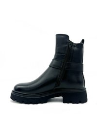 Stivale alla caviglia in pelle nera con chiusura a zip, texture liscia, con cinturini in evidenza e suola in gomma spessa e scanalata.