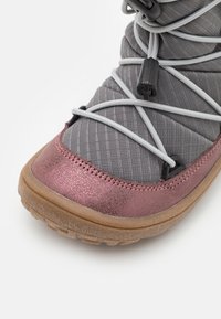 Grijze stoffen bovenkant van de schoen met metallic roze afwerking, voorzien van grijze veters en plastic accenten. De zool is lichtbruin met een gestructureerd oppervlak.