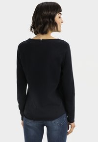 Marineblauwe longsleeve top met een ronde halslijn en een kleine metalen accent aan de achterkant, gemaakt van een zachte, gestructureerde stof.