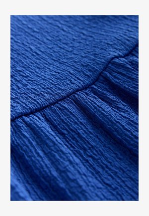 Țesătură texturată albastră cu suprafață creponată, prezentând valuri distincte și pliuri, indicând un material ușor și fluid.