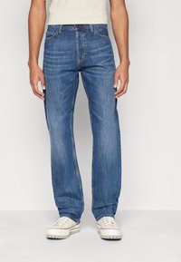 Světle modré džínové kalhoty s rovnými nohavicemi, zapínáním na knoflík, pěti kapsami a jemným vyblednutím. Kombinovány s bílými teniskami.