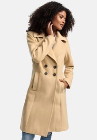 Beige dubbelbreasted coat met grote revers, knopenlijst aan de voorkant, zijzakken en verticale ribbelaccenten. Zachte stof met een gestructureerde pasvorm.